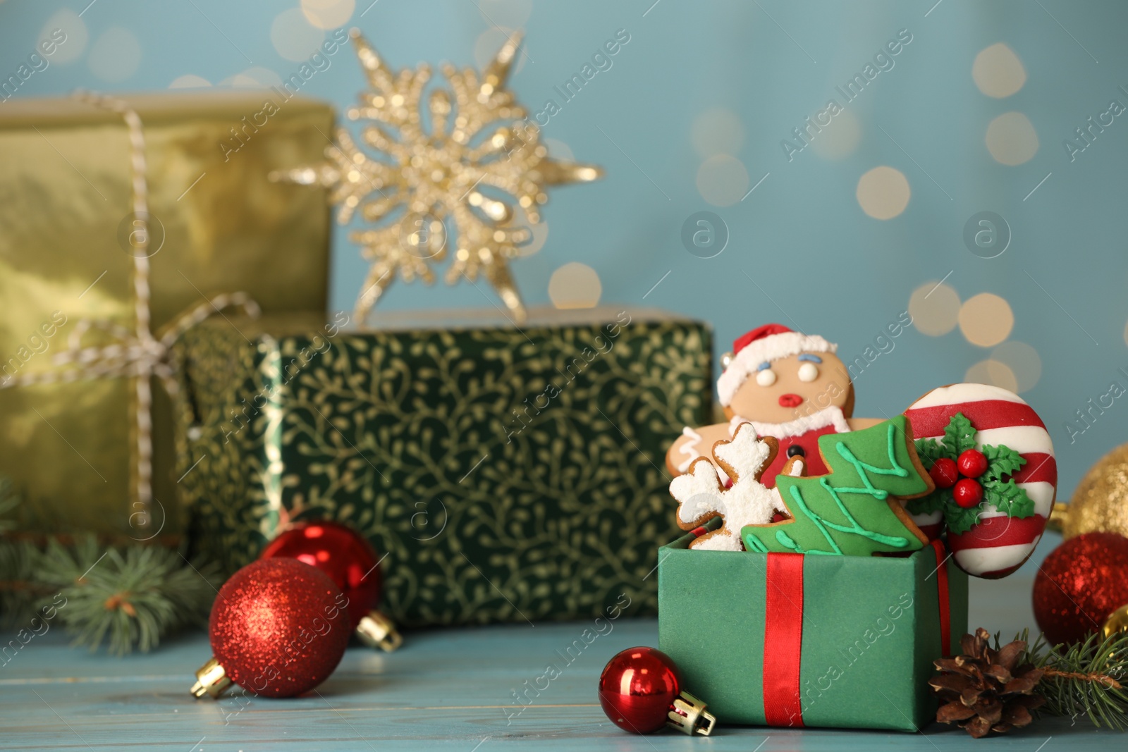 Photo of Sweet Christmas cookies and decor on light blue table against blurred festive lights. Space for text