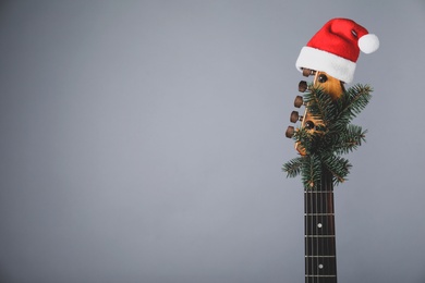 Photo of Guitar with Santa hat and fir tree branch on grey background, space for text. Christmas music