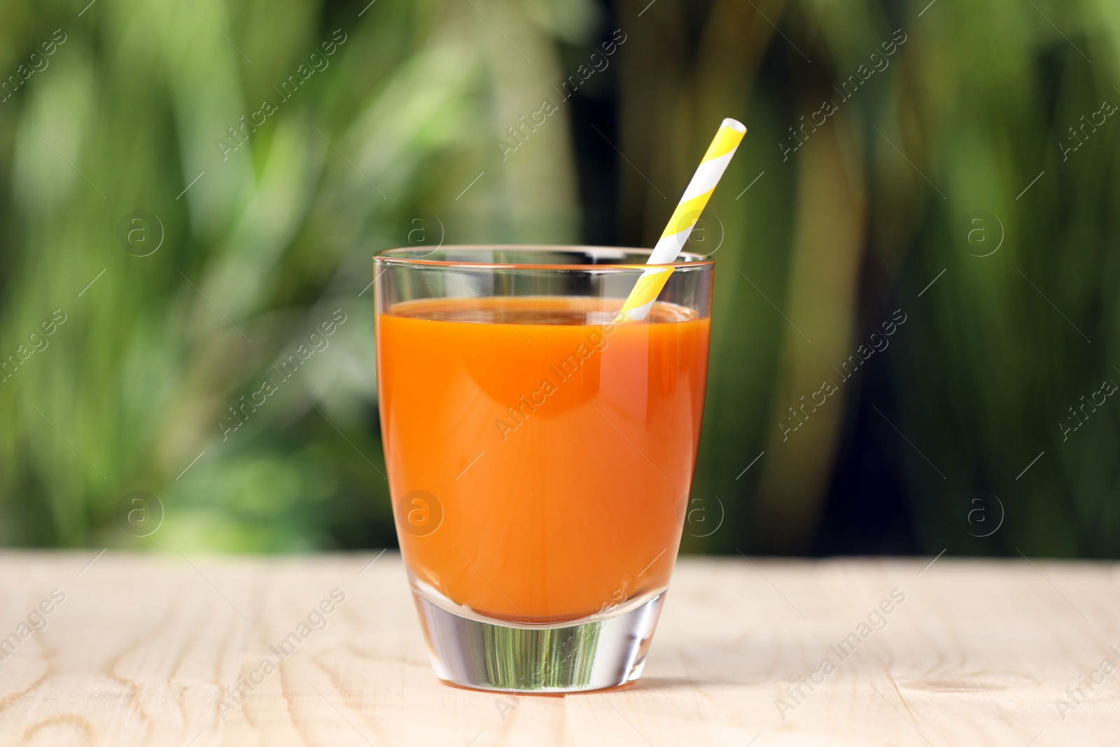 Photo of Glass of tasty carrot juice on wooden table outdoors, closeup