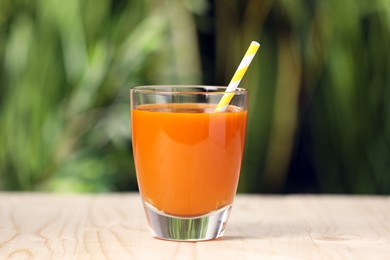 Glass of tasty carrot juice on wooden table outdoors, closeup