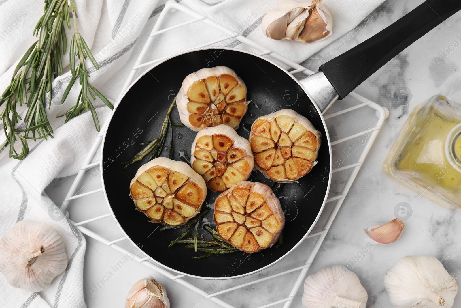 Photo of Frying pan with fried garlic, rosemary and oil on light table, flat lay