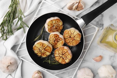 Photo of Frying pan with fried garlic, rosemary and oil on light table, flat lay