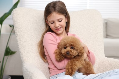 Little child with cute puppy in armchair at home. Lovely pet