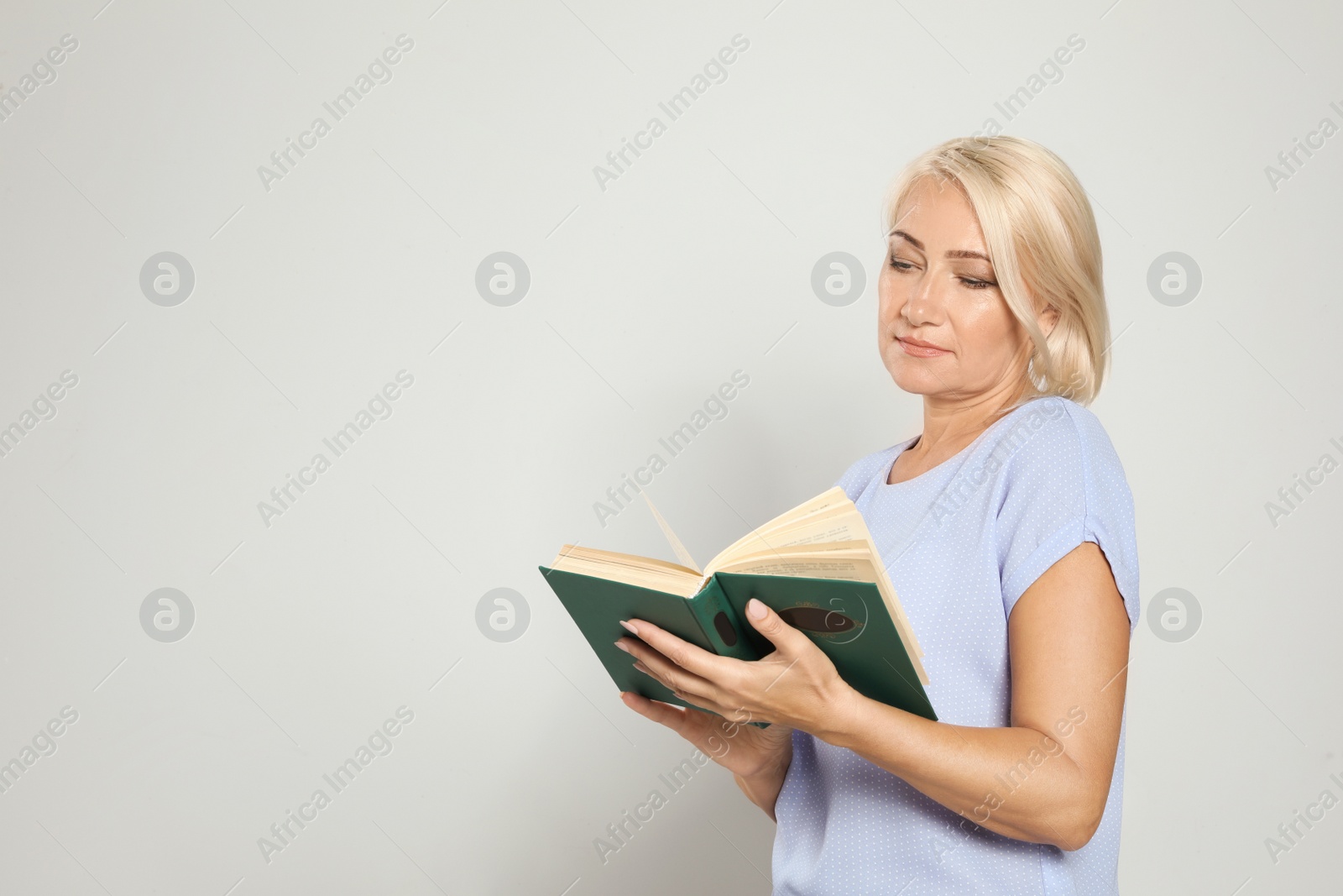 Photo of Mature woman reading book on light background, space for text