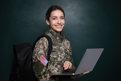 Photo of Female cadet with backpack and laptop near chalkboard. Military education