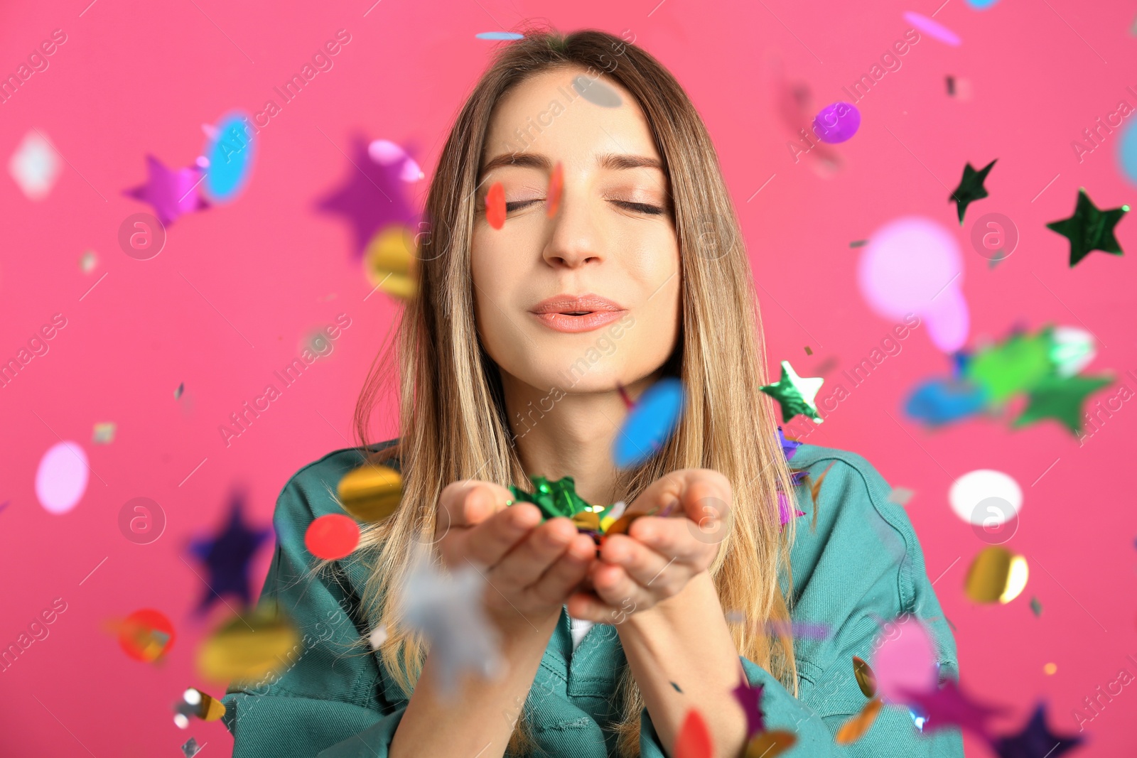 Photo of Happy woman blowing confetti on pink background