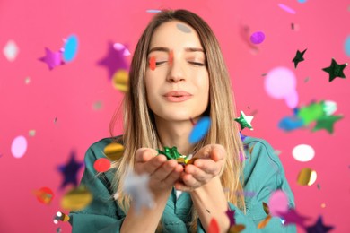 Photo of Happy woman blowing confetti on pink background