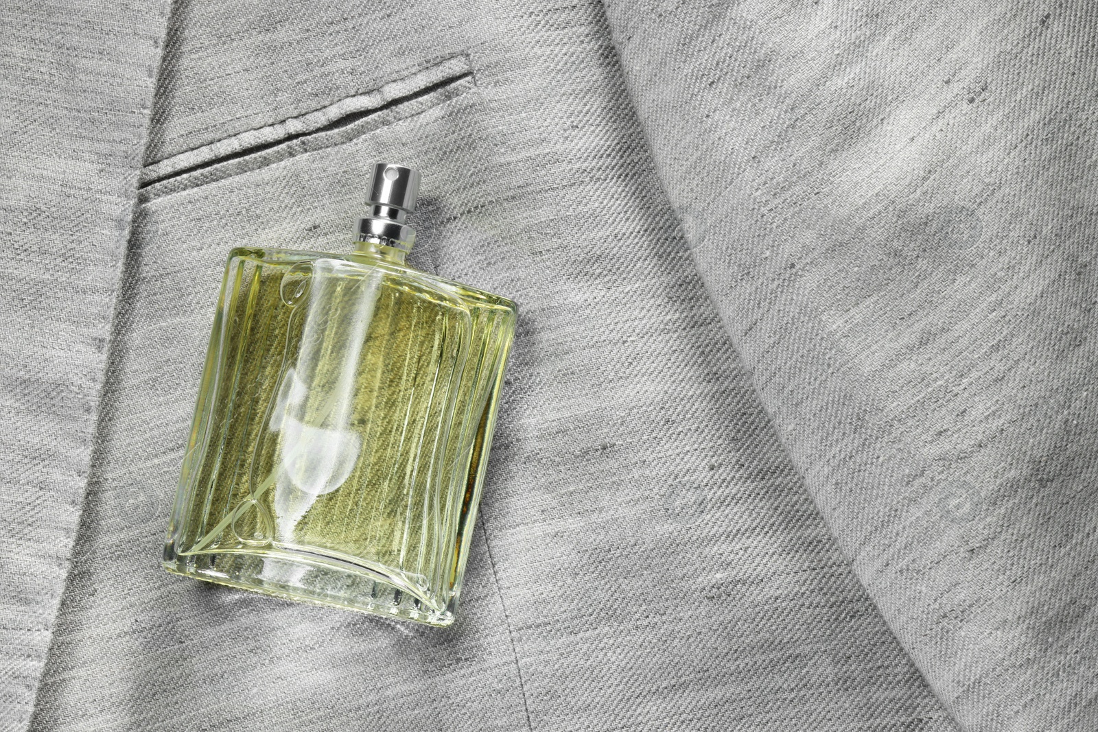 Photo of Luxury men's perfume in bottle on grey jacket, top view. Space for text