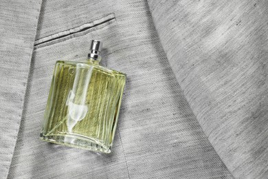 Photo of Luxury men's perfume in bottle on grey jacket, top view. Space for text