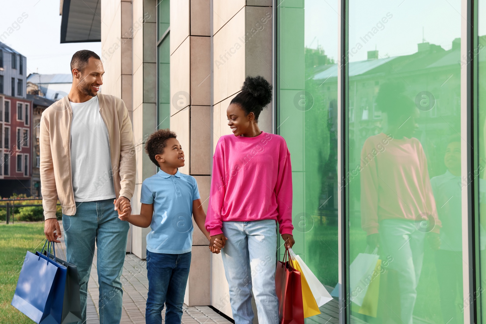 Photo of Family shopping. Happy parents and son with colorful bags near mall outdoors