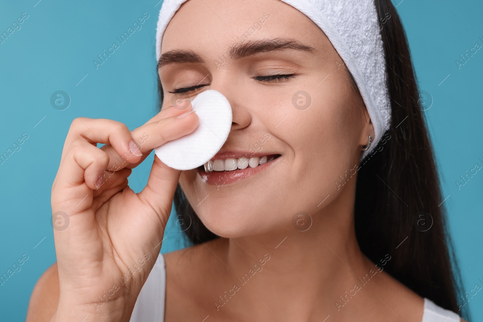 Photo of Young woman with cotton pad on light blue background, closeup