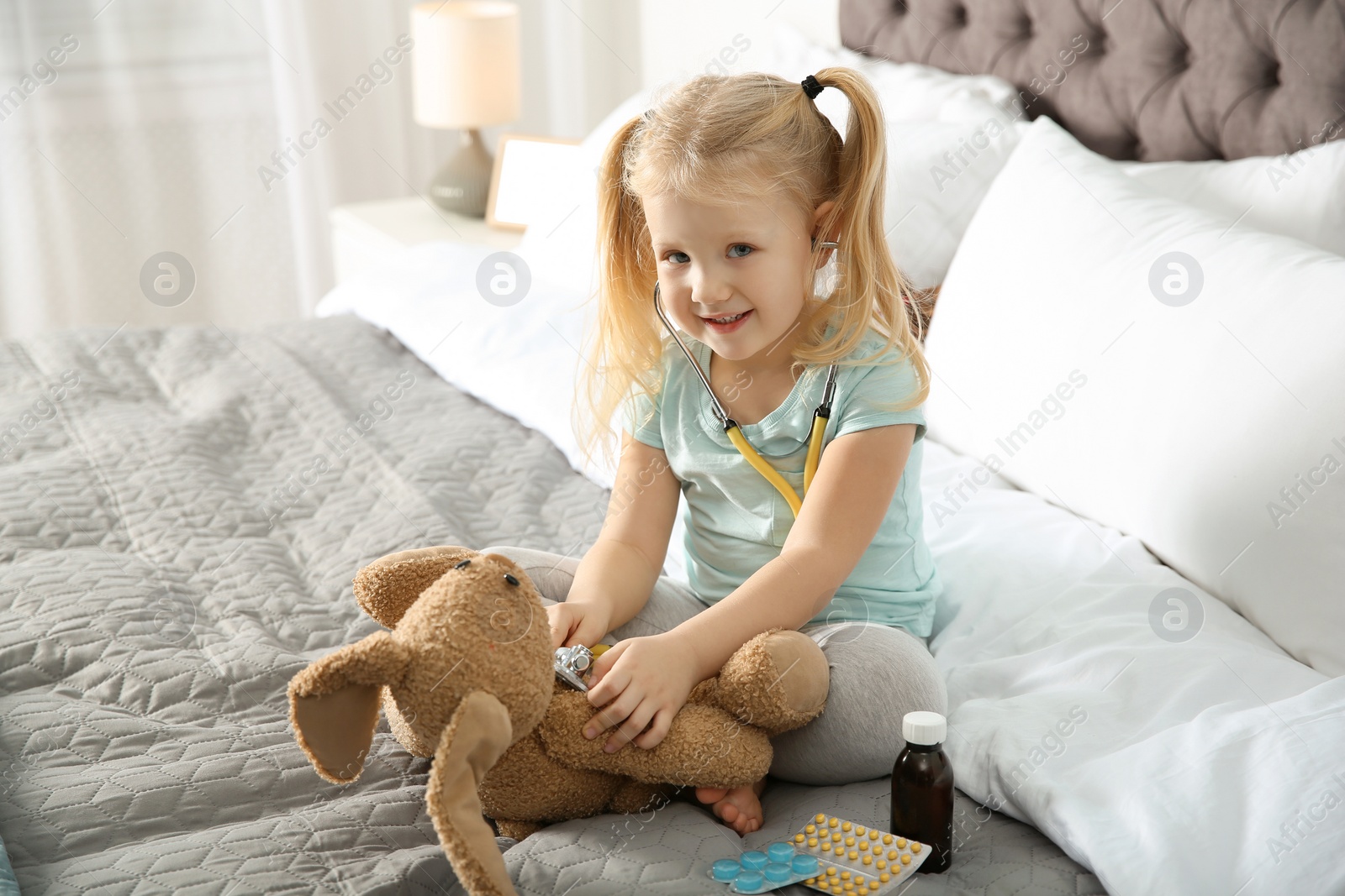 Photo of Cute child imagining herself as doctor while playing with stethoscope and toy bunny at home