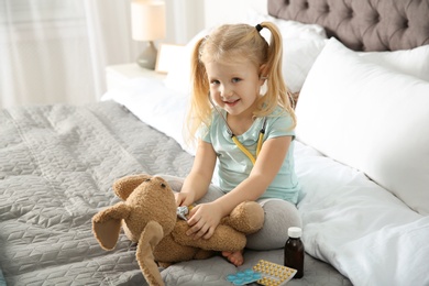 Cute child imagining herself as doctor while playing with stethoscope and toy bunny at home