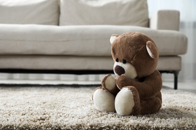 Photo of Cute lonely teddy bear on floor near sofa in room. Space for text