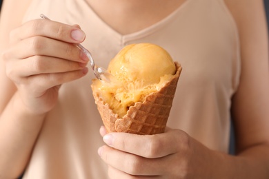 Woman eating yellow ice cream in wafer cone, closeup