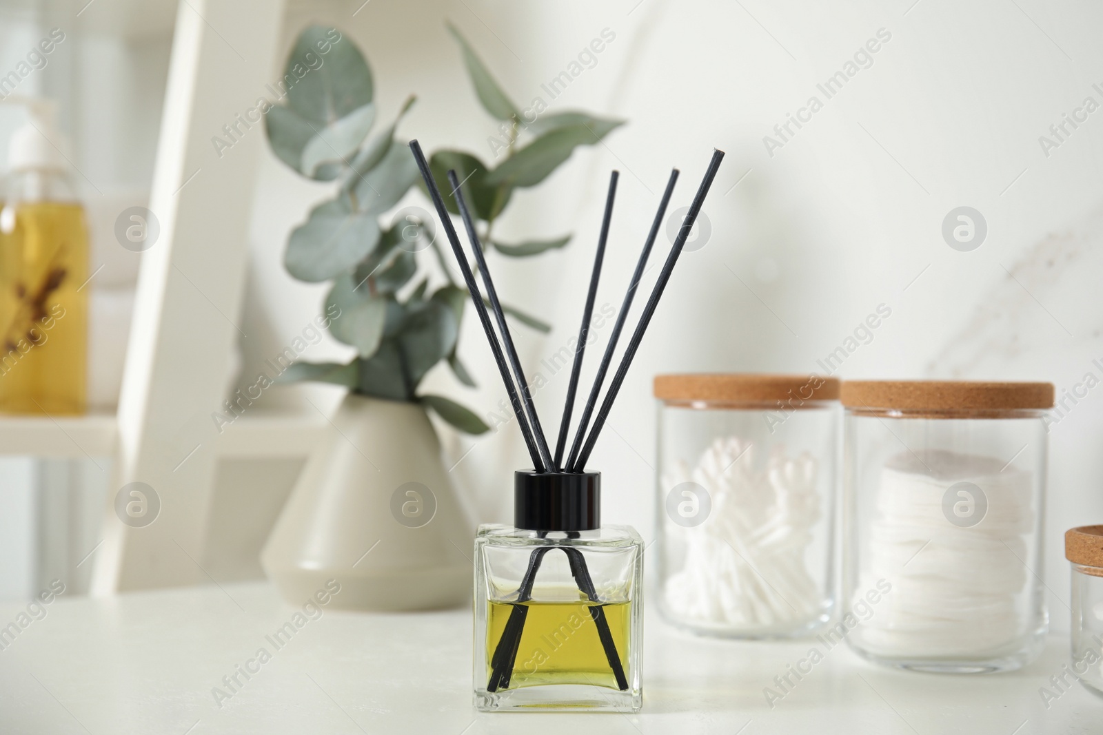 Photo of Aromatic reed air freshener and toiletries on white countertop in bathroom