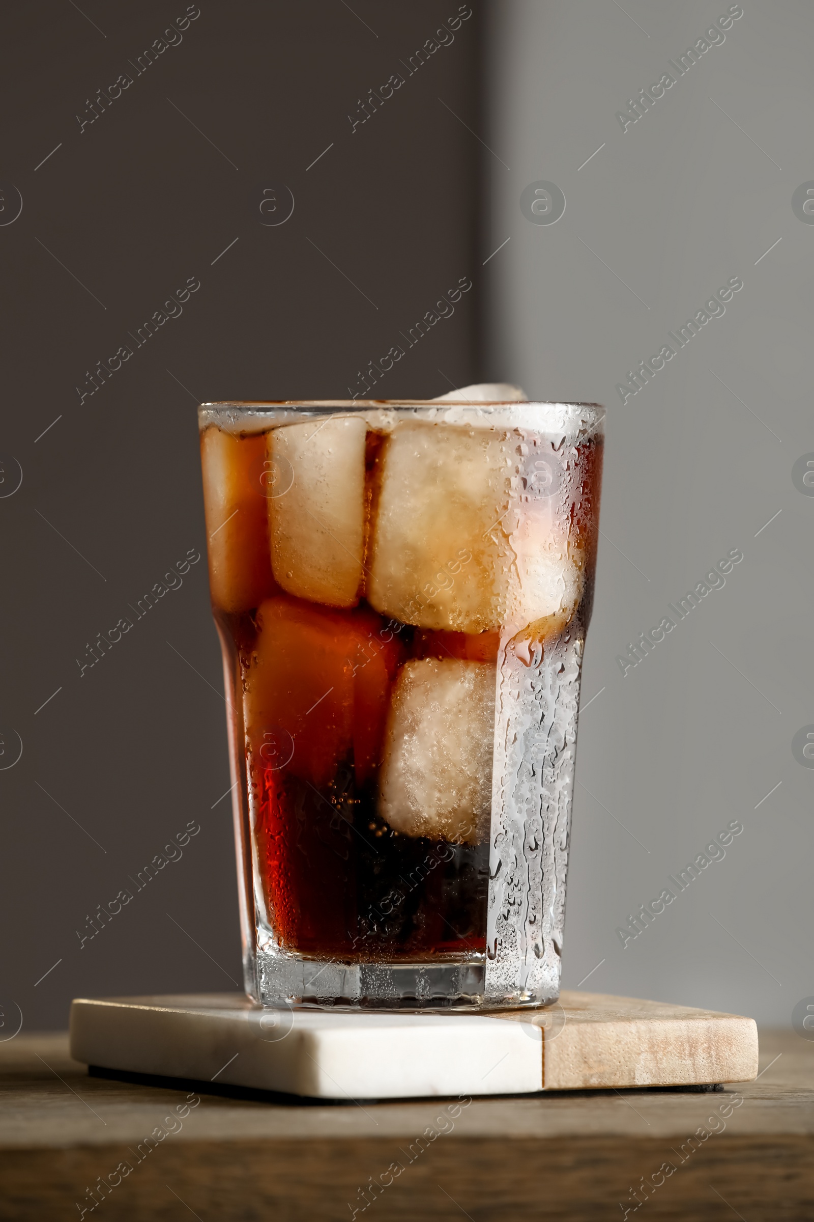 Photo of Glass of cold drink and stylish cup coaster on wooden table in room