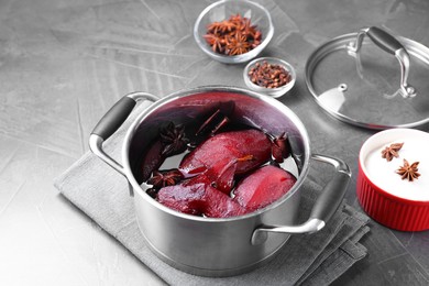Tasty red wine poached pears and spices in pot on grey table