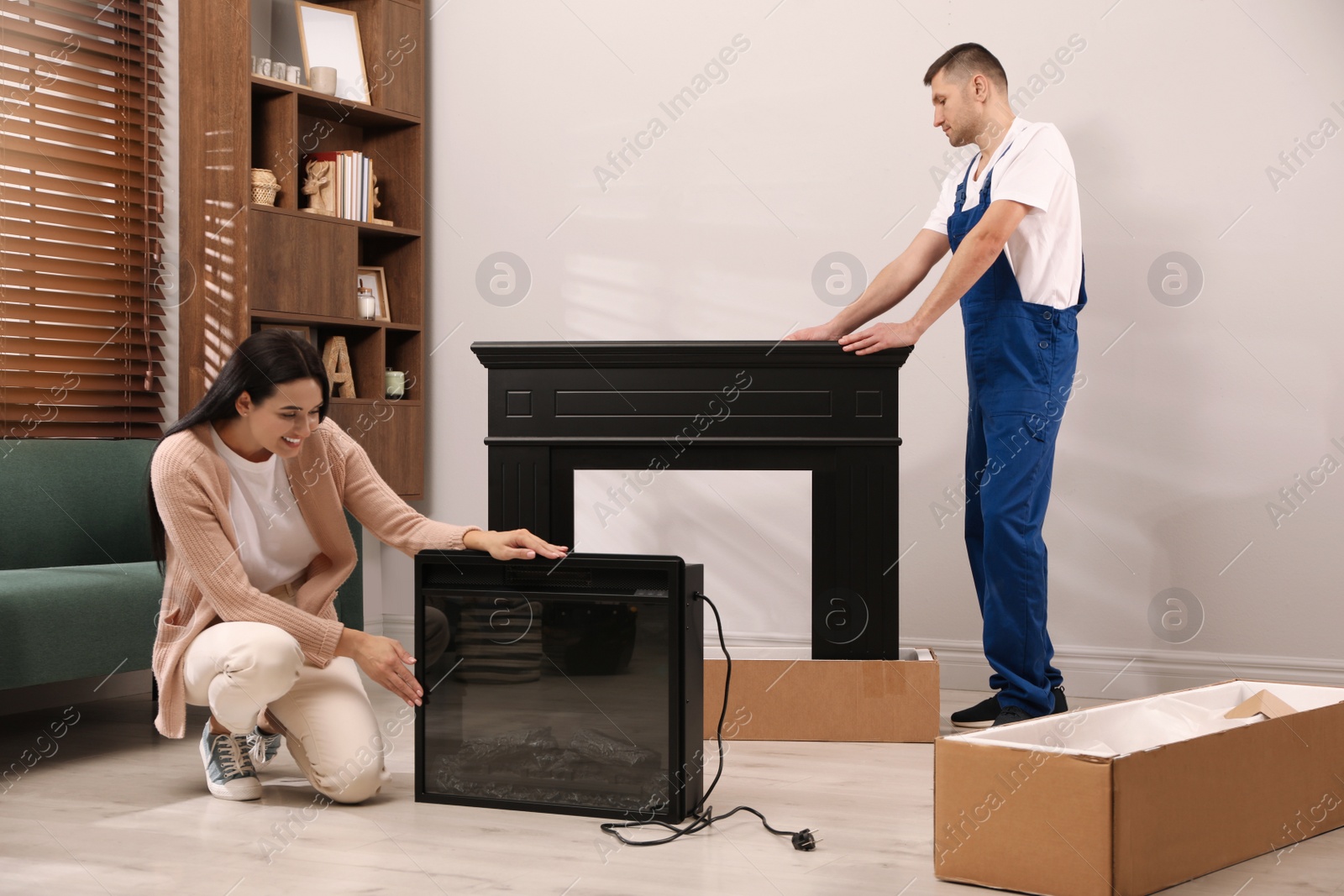 Photo of Young woman and professional technician with electric fireplace in room. Installing heater