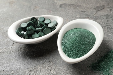 Dishes of spirulina pills and powder on color background, closeup