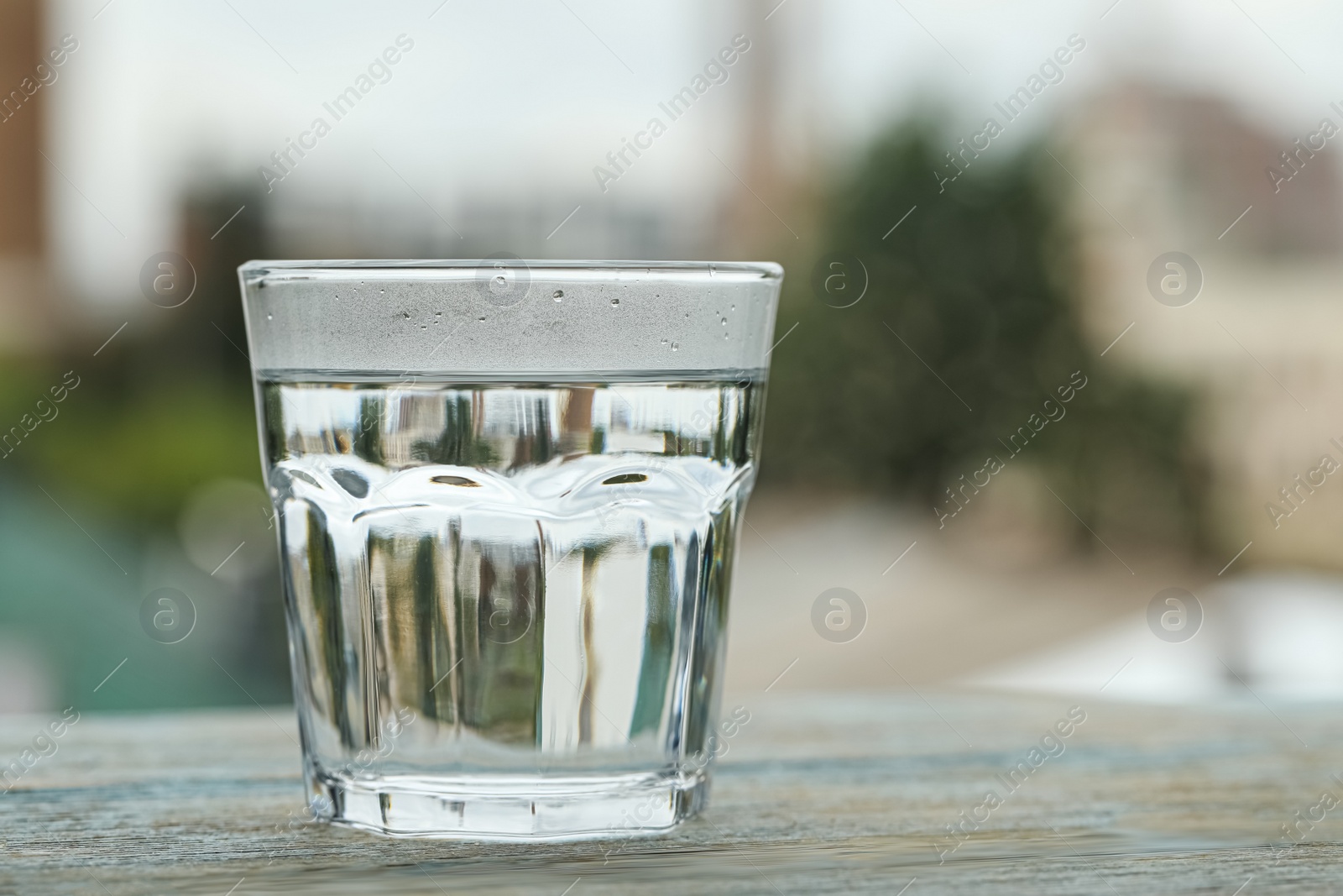 Photo of Glass of pure water on light blue wooden table against blurred background, space for text