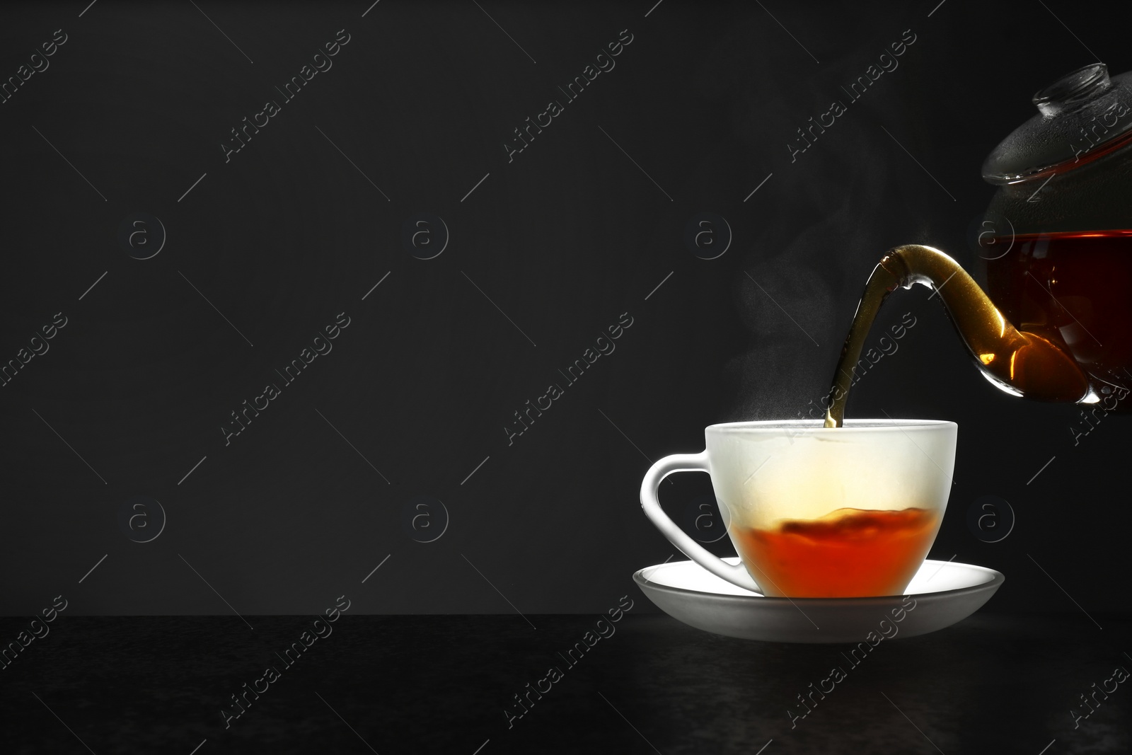 Photo of Pouring fresh hot tea into glass cup on table against grey background, space for text