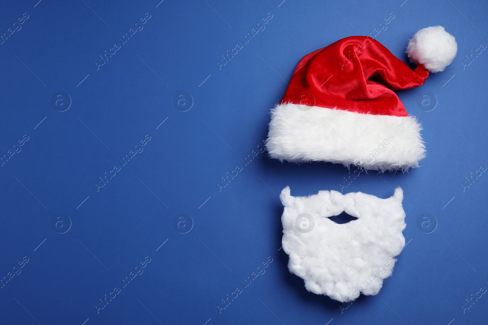 Photo of Santa Claus hat and beard on blue background, flat lay. Space for text