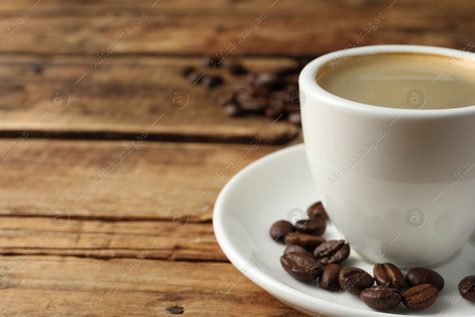 Photo of Cup of hot aromatic coffee and roasted beans on wooden table, space for text