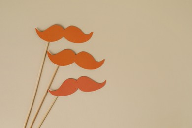 Fake paper mustaches party props on beige background, flat lay. Space for text