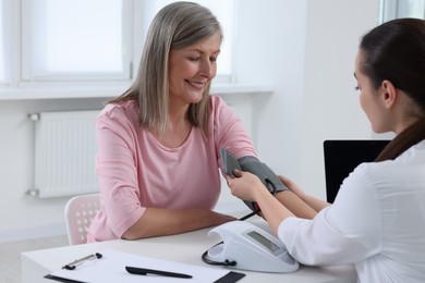 Doctor measuring blood pressure of woman at table indoors