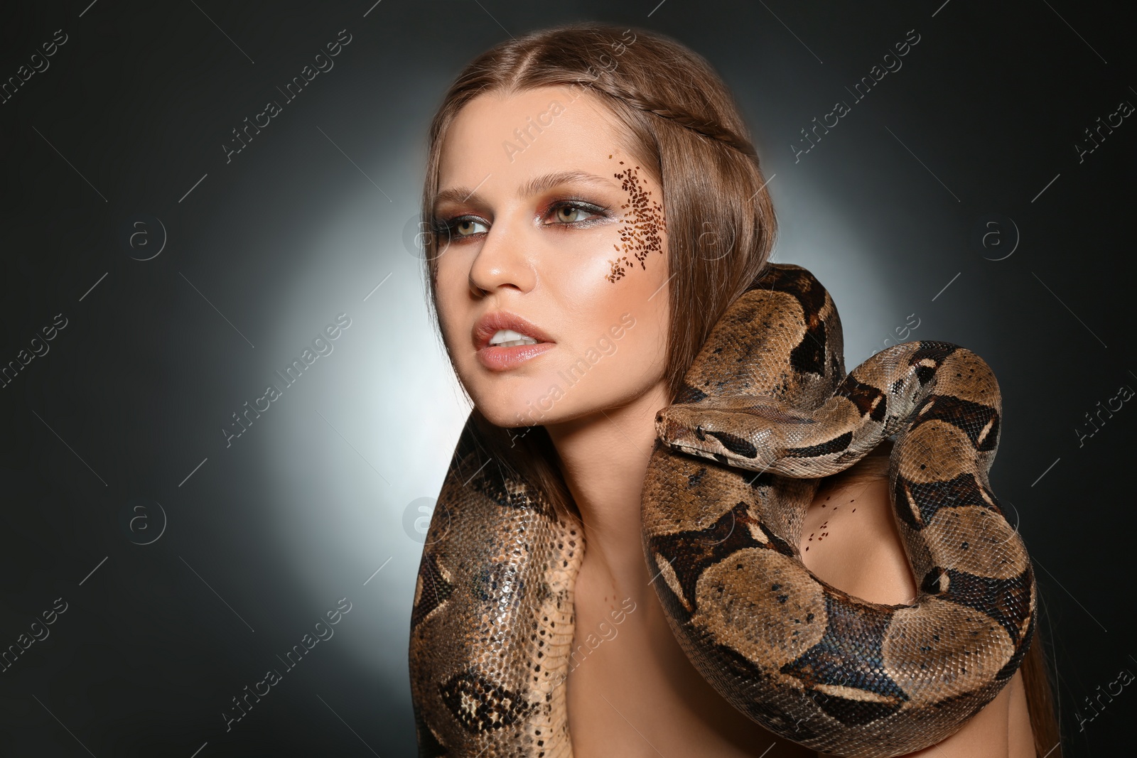 Photo of Beautiful woman with boa constrictor on dark background