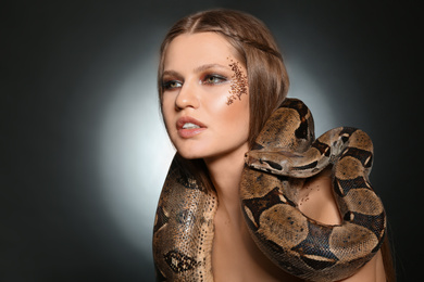 Photo of Beautiful woman with boa constrictor on dark background