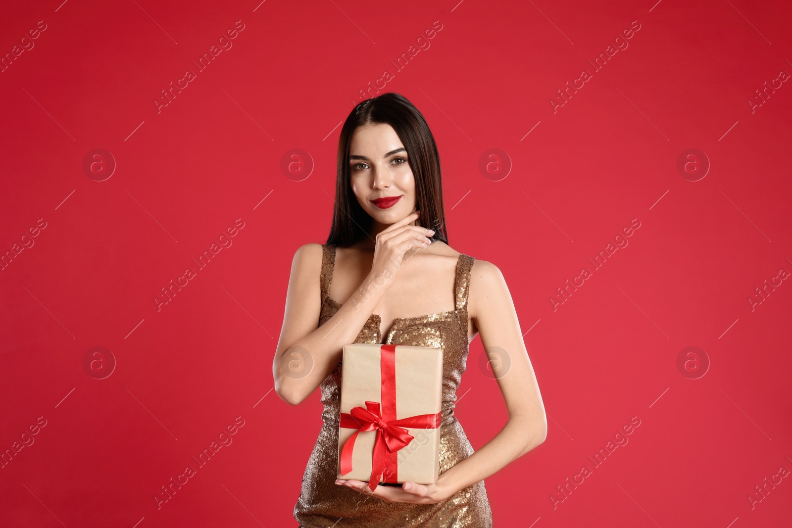 Photo of Woman in golden dress holding Christmas gift on red background