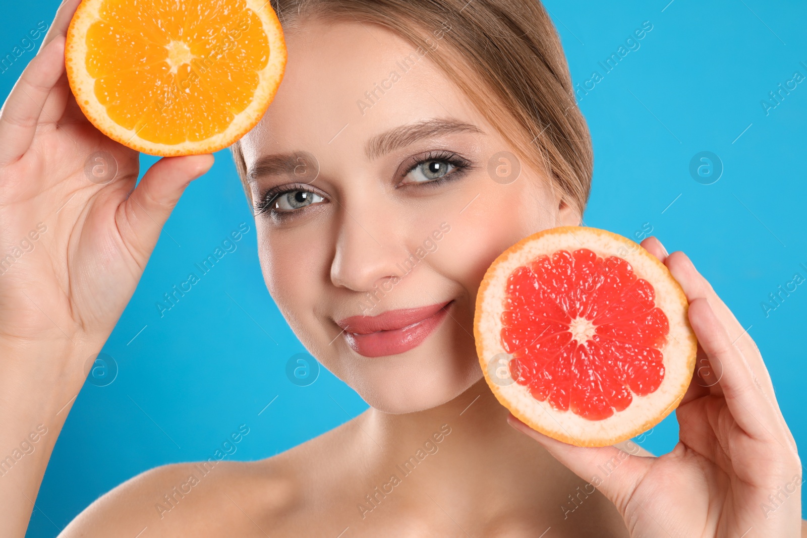 Photo of Young woman with cut grapefruit and orange on blue background. Vitamin rich food