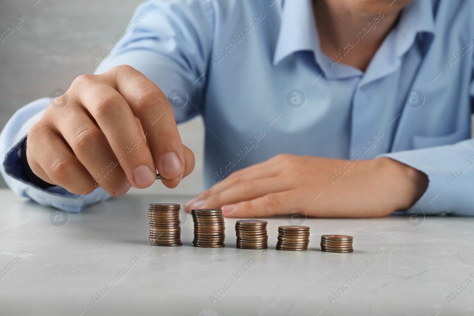 Photo of Man stacking coins on grey stone table, closeup view