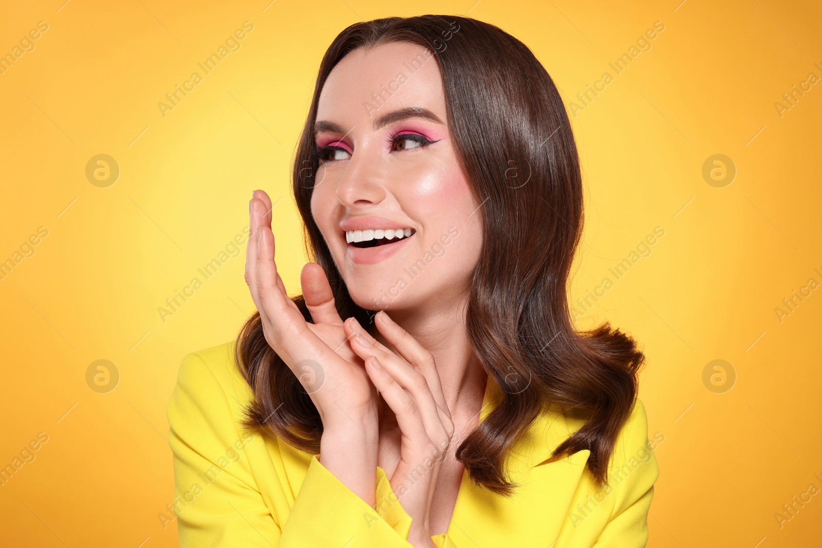 Photo of Portrait of beautiful young woman with makeup and gorgeous hair styling on yellow background