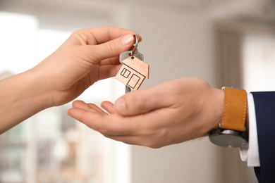 Photo of Real estate agent giving key with trinket to client in office, closeup