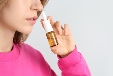 Photo of Sick young woman using nasal spray on white background, closeup