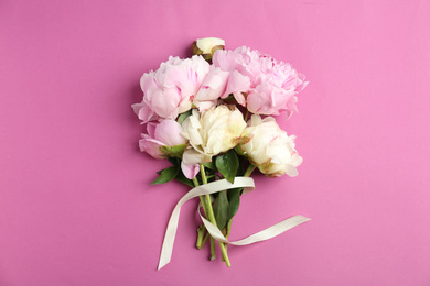 Bouquet of beautiful peonies with ribbon on pink background, flat lay