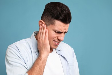 Man suffering from ear pain on light blue background. Space for text