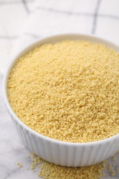 Photo of Raw couscous in bowl on light table, closeup