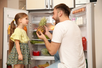 Photo of Young father and daughter with fresh pineapple near refrigerator at home