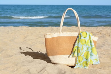 Photo of Straw bag with beach wrap on sandy seashore, space for text. Summer accessories