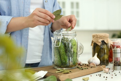 Woman putting bay leaves into pickling jar at table in kitchen, closeup