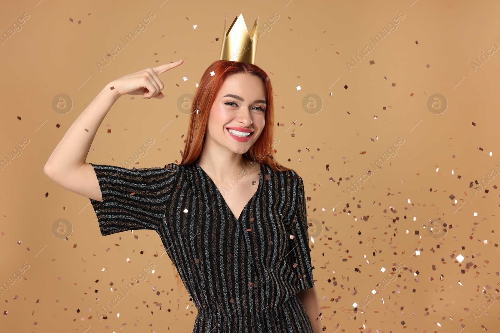 Photo of Beautiful young woman with princess crown under falling confetti on beige background, space for text