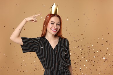 Photo of Beautiful young woman with princess crown under falling confetti on beige background, space for text