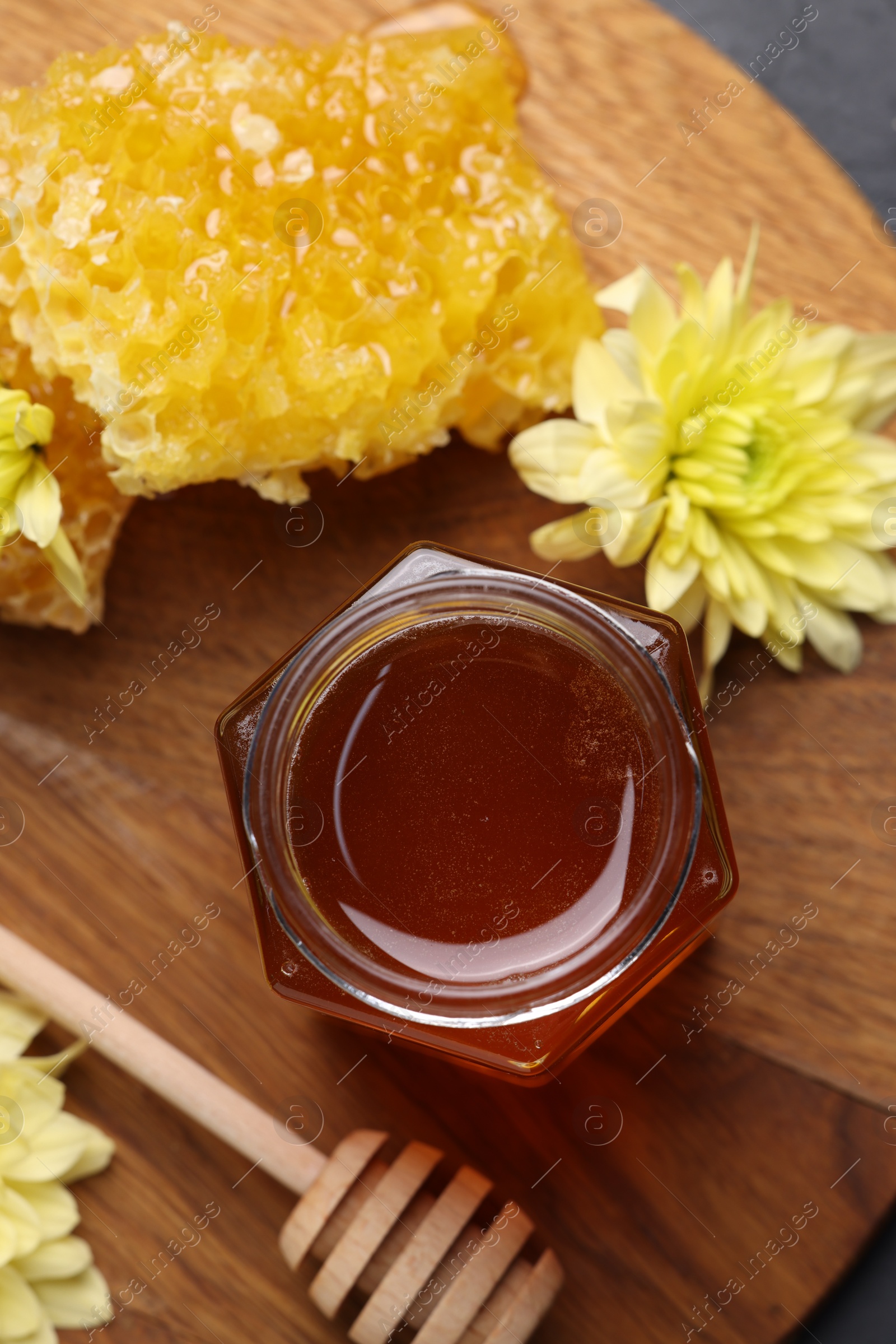 Photo of Sweet honey in jar, dipper, chrysanthemum flowers and pieces of honeycomb on table, flat lay