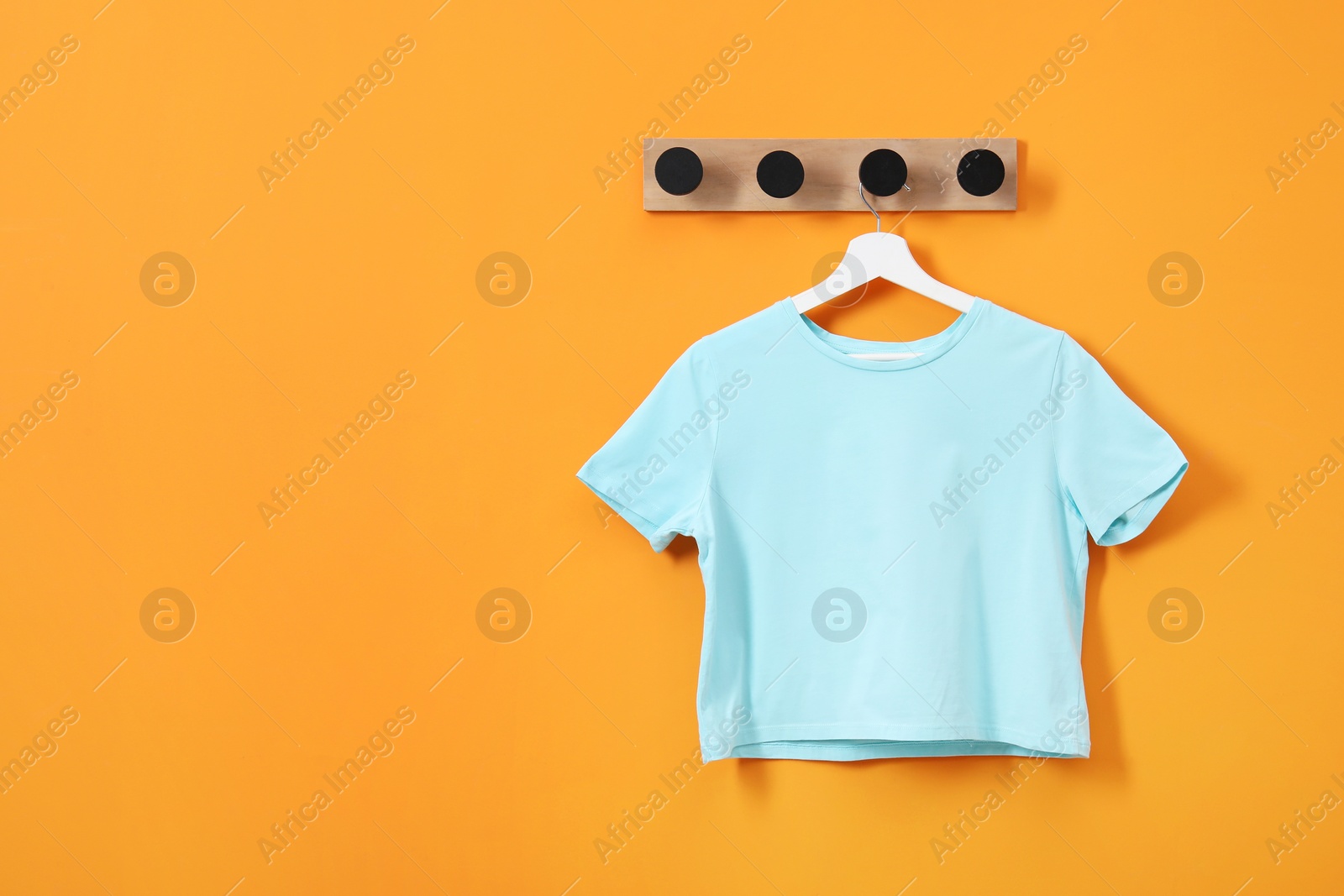 Photo of Hanger with light blue T-shirt on orange wall, space for text