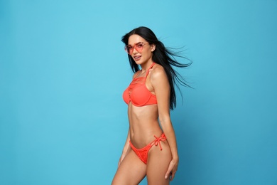 Photo of Beautiful young woman in stylish bikini with sunglasses on light blue background