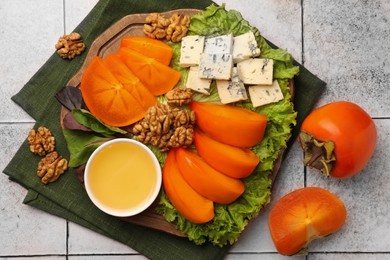 Delicious persimmon, blue cheese, nuts and honey served on tiled surface, flat lay